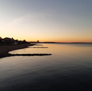 Die Ostsee im Abendlicht, links der Strand, rechts das Wasser, die Wellenbrecher reihen sich aneinander, Himmel und Meer sind blau bis gelb