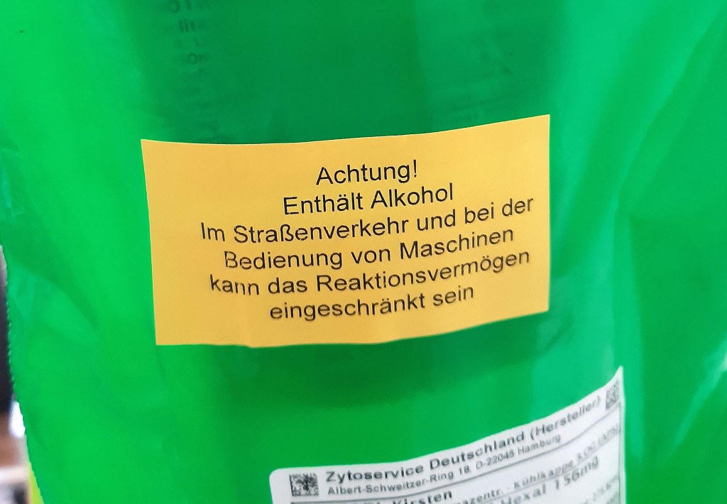 Grüner Plastikbeutel mit einem Chemo-Medikament, darauf klebt ein gelber Aufkleber mit der Warnung: "Achtung! enthält Alkohol - im Straßenverkehr und bei der Bedienung von Maschinen kann das Reaktionsvermögen eingeschränkt sein"